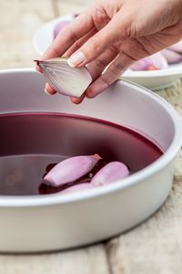 Cropped hand of woman putting onion in red wine on table