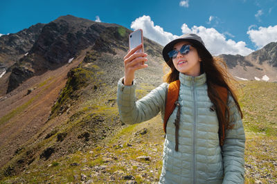 Beautiful happy hiker woman taking a selfie hiking a mountain at vacation. girl wearing hat and