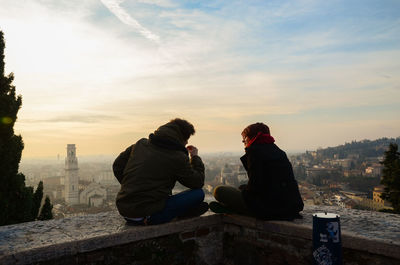 Friends sitting on rock against sky during sunset