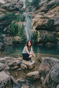 Portrait of young woman sitting on rock at shore