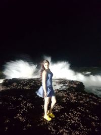 Young woman standing by sea against sky at night