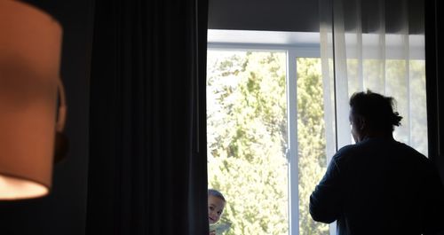 Rear view of man looking through window at home