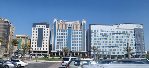 Cars on road by buildings against clear blue sky