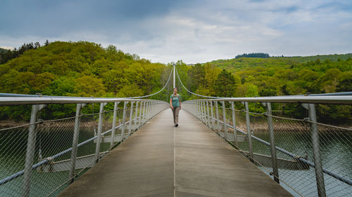 Rear view of man walking on footbridge against sky