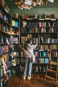 Rear view of girl choosing books from shelf in bookstore