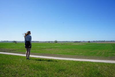 Rear view full length of woman standing on field against clear blue sky