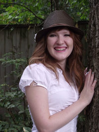 Young woman wearing hat standing by tree trunk in park