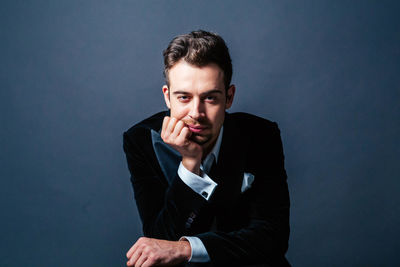 Portrait of young man sitting against gray background