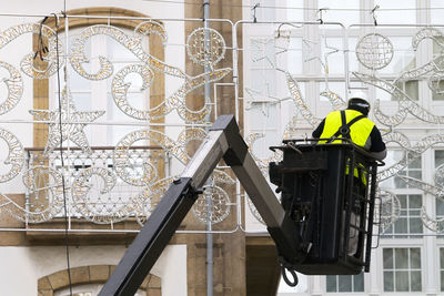 Unrecognizable electrician worker in bucket installing christmas lights in city street on crane