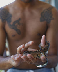 Midsection of shirtless man holding snake