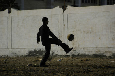 Boy playing soccer on field against wall