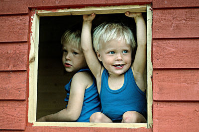 Sibling looking through wooden window of playhouse