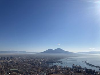 Aerial view of city by mountains against clear blue sky