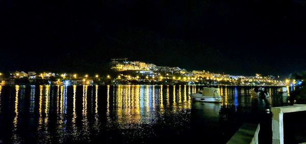 Illuminated city by river against sky at night