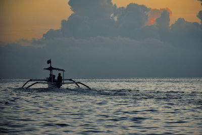 Silhouette boat on sea against cloudy sky during sunset