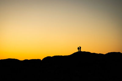 Silhouette man standing on mountain against clear sky during sunset