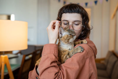 Cat owner caring woman hug kissing holding in hands loving pet at home. therapy by domestic animal