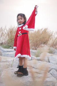 Portrait of cute girl wearing red dress while standing on rocks against sky