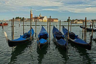 Gondolas moored in canal against cloudy sky