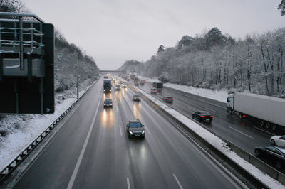 Vehicles on highway against sky during winter