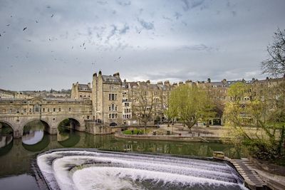 River by bridge and buildings against cloudy sky