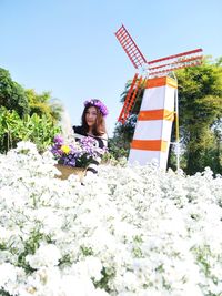 Woman sitting on flowering plant against sky