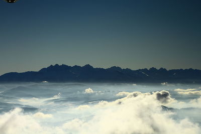 Scenic view of cloud covered mountains against clear sky at dusk