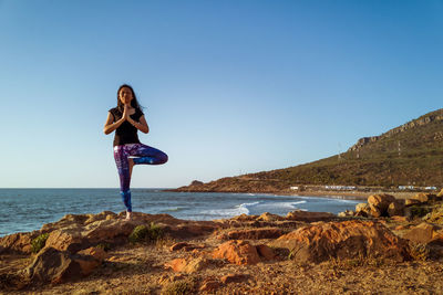 Man standing on rock at beach against clear sky