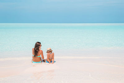 Friends sitting on beach against sky