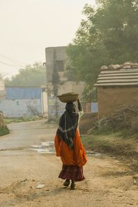 Full length rear view of woman carrying bucket on head in village