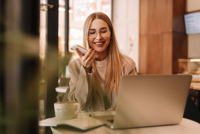 A young millennial student records a voice message and studies online using a laptop and smartphone