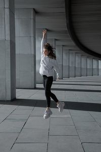 Young woman with arm raised jumping in corridor