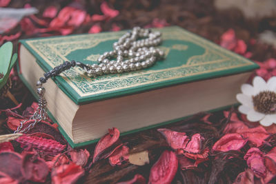 Close-up of koran with prayer beads and flowers on table