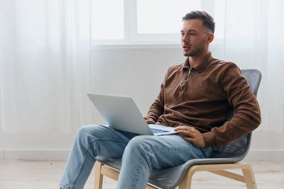 Young man using laptop while sitting on sofa at home