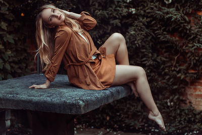 Portrait of sensual fashion model sitting on stone table against plants in back yard