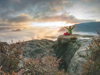 Man on rock against sky during sunset