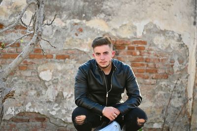 Portrait of young man sitting against brick wall