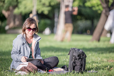 Woman using digital tablet while sitting on grass at park