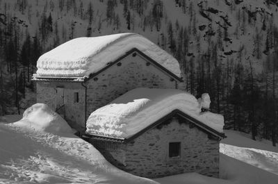 Snow covered house by tree and mountain during winter