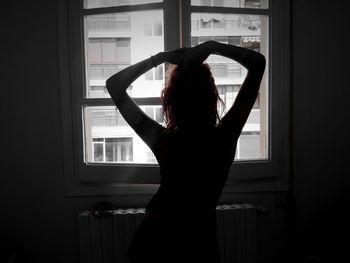 Rear view of silhouette woman standing against window