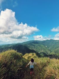 Rear view of woman standing by grass against mountains and sky