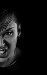 Close-up portrait of angry young woman against black background