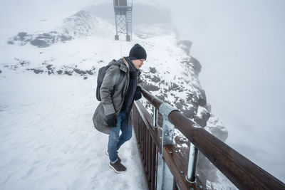 Young man standing on snow covered mountain by railing