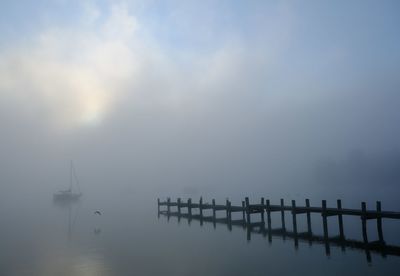 Silhouette wooden posts in sea against sky during foggy weather