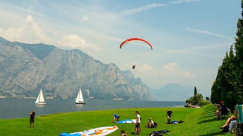 People with paragliding equipment by lake against mountain