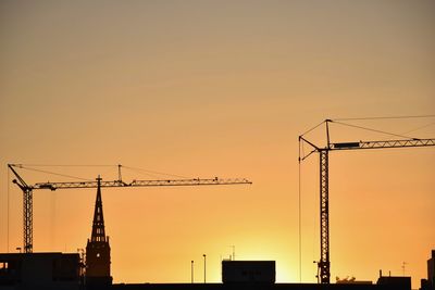 Low angle view of silhouette cranes against orange sky