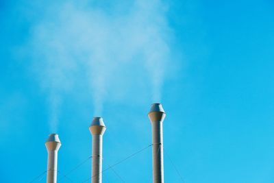 Low angle view of smoke emitting from chimney against blue sky