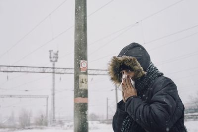 Portrait of woman sneezing against sky during winter