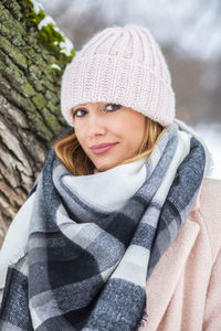 Portrait of young woman standing by tree trunk during winter