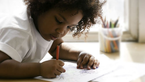 Little african girl painting and drawing on paper. preschool girl lying writing on floor.